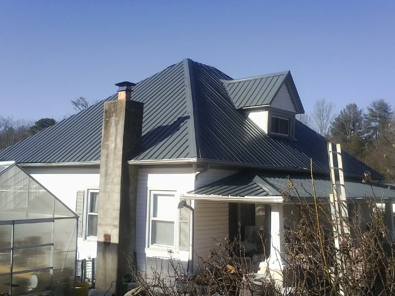 Dark blue standing seam metal roof on a white farmhouse with dormer — Slate & Tile Roof Repair by Roofing Brothers in Chatham