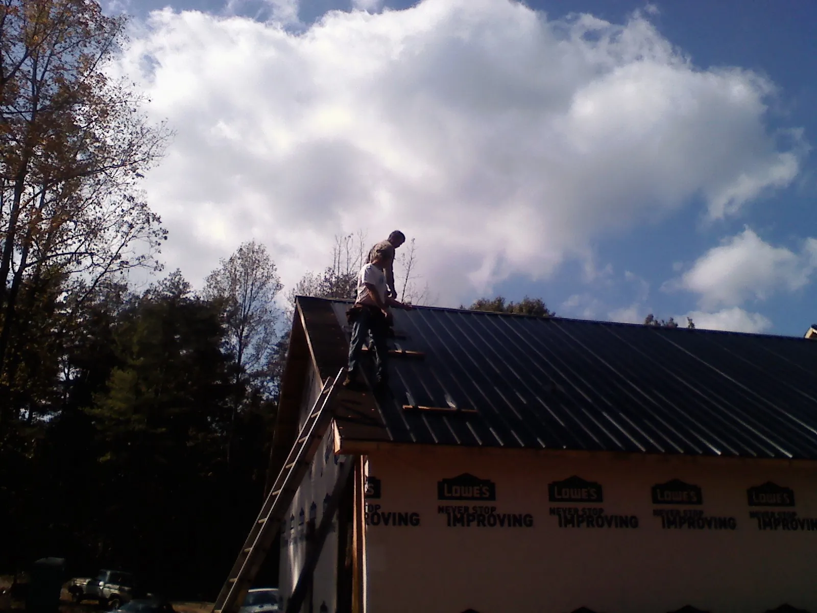 Roofer fastening dark metal panels high against a cloudy sky, from a Roof Inspection job in Chatham