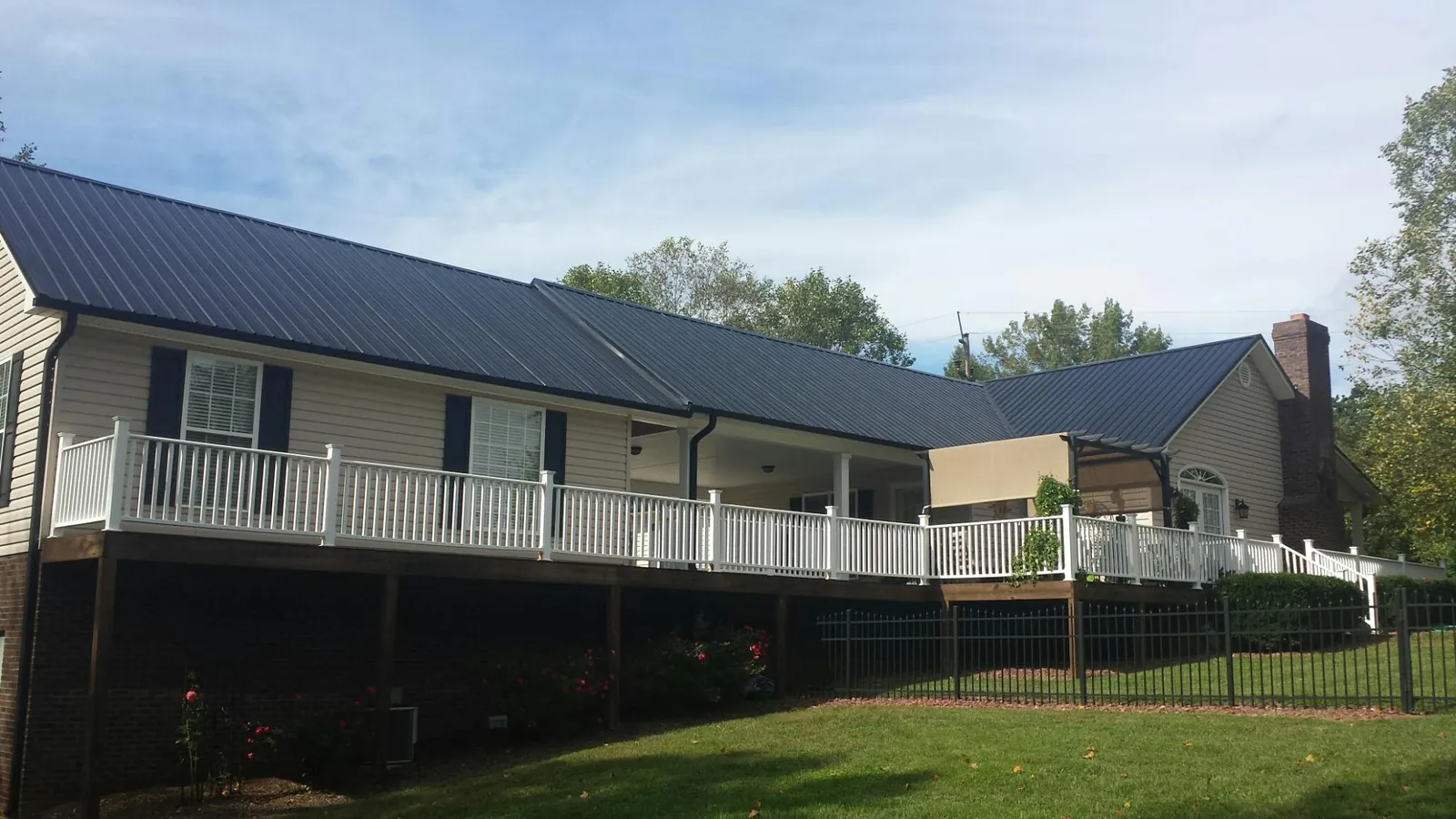 Black metal roof above a long white railed deck on a hillside home in Chatham